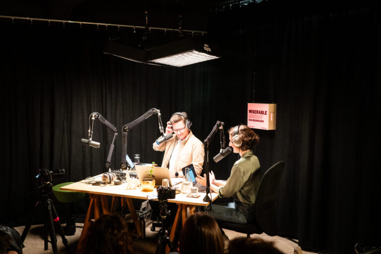 Ein Mann und eine Frau mit Kopfhörern zwischen Mikros in einem Aufnahmestudio