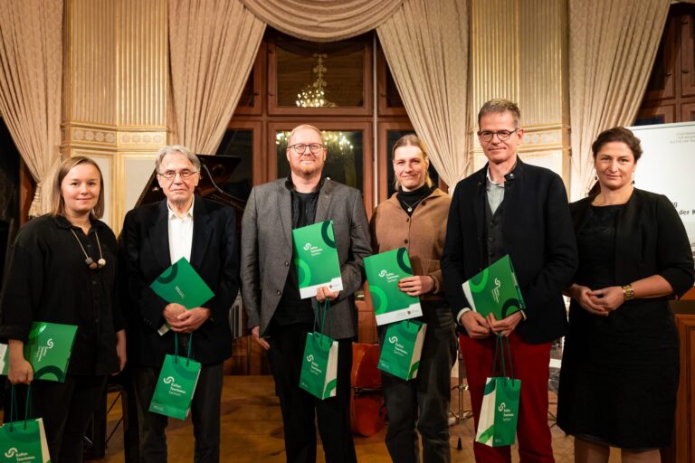Sechs weiße Menschen, drei Frauen und drei Männer, alle schick gekleidet. Fünf Menschen halten eine grüne Urkunde und grüne Taschen in der Hand mit der Aufschrift: Kultur Tourismus Sachsen.